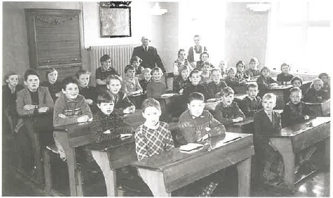 Lærer Fabricius med hele skolen ca. 1955. Klasseværelset er pyntet i anledning af hans fødselsdag, og hans kone med forklæde er parat til at servere kage og saftevand for eleverne.